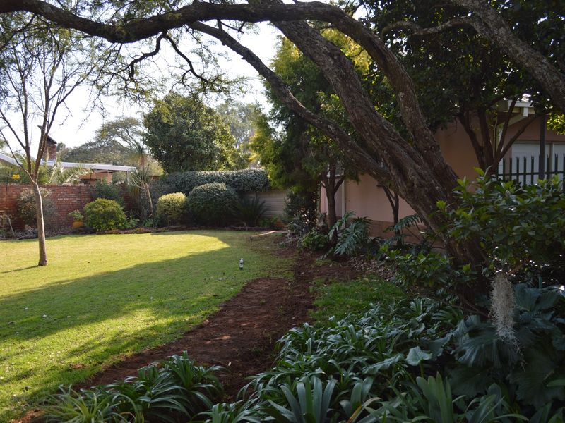 A spacious rear garden featuring a well-maintained lawn, mature trees, and established garden beds enclosed by a brick boundary wall.