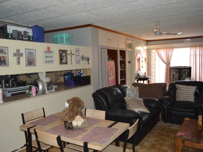 Open-plan living and dining area featuring a pass-through kitchen counter, ceiling fan, and tiled flooring, offering a functional layout with potential for modernization.