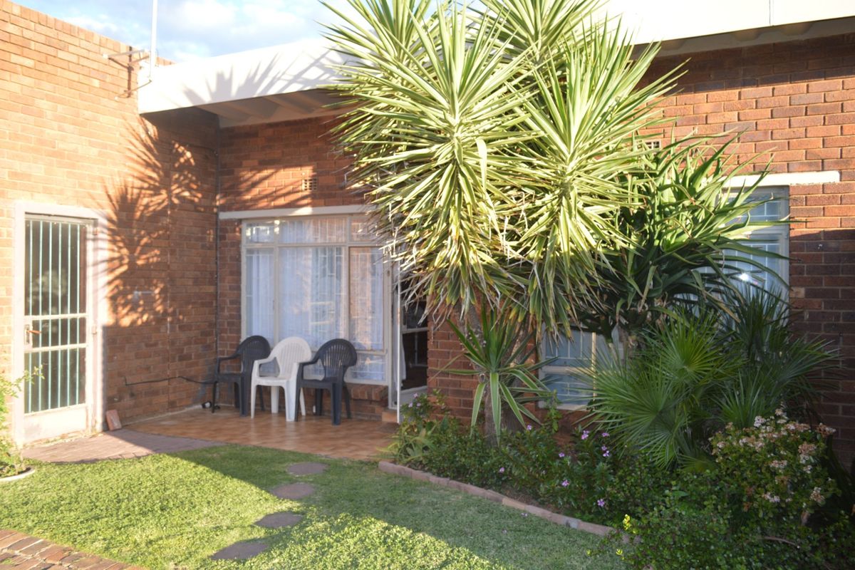 Rear view of the townhouse featuring a brick facade, a tiled patio area, and established garden landscaping.