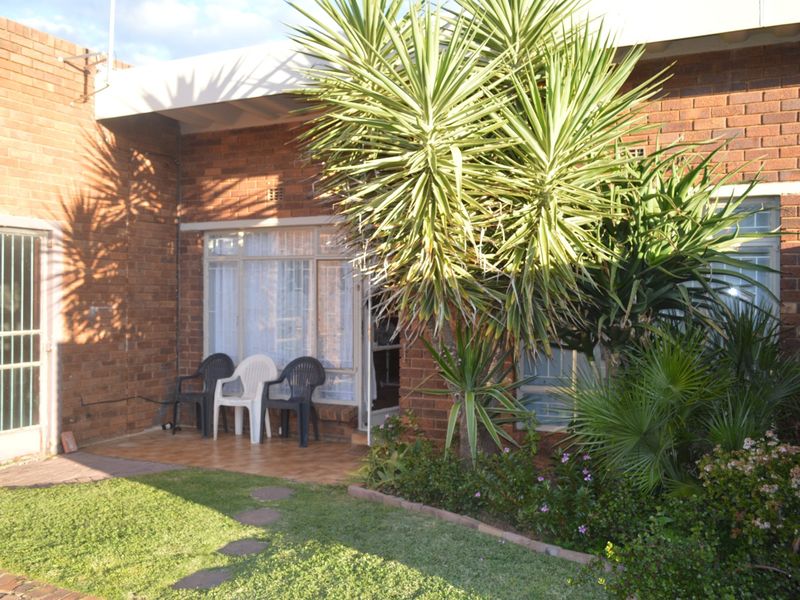 Rear view of the townhouse featuring a brick facade, a tiled patio area, and established garden landscaping.