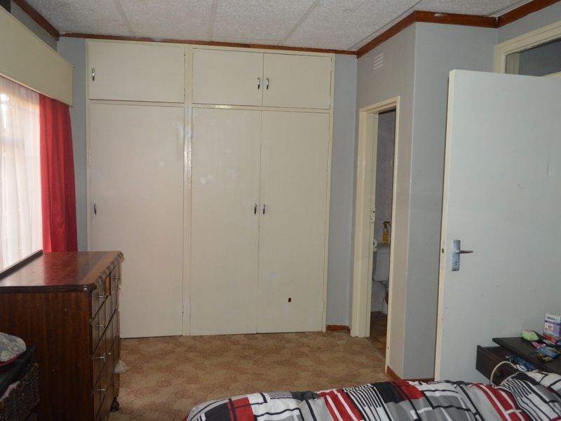 A bedroom featuring built-in cupboards, carpeted flooring, and a drop ceiling, with an adjacent doorway leading to a bathroom.