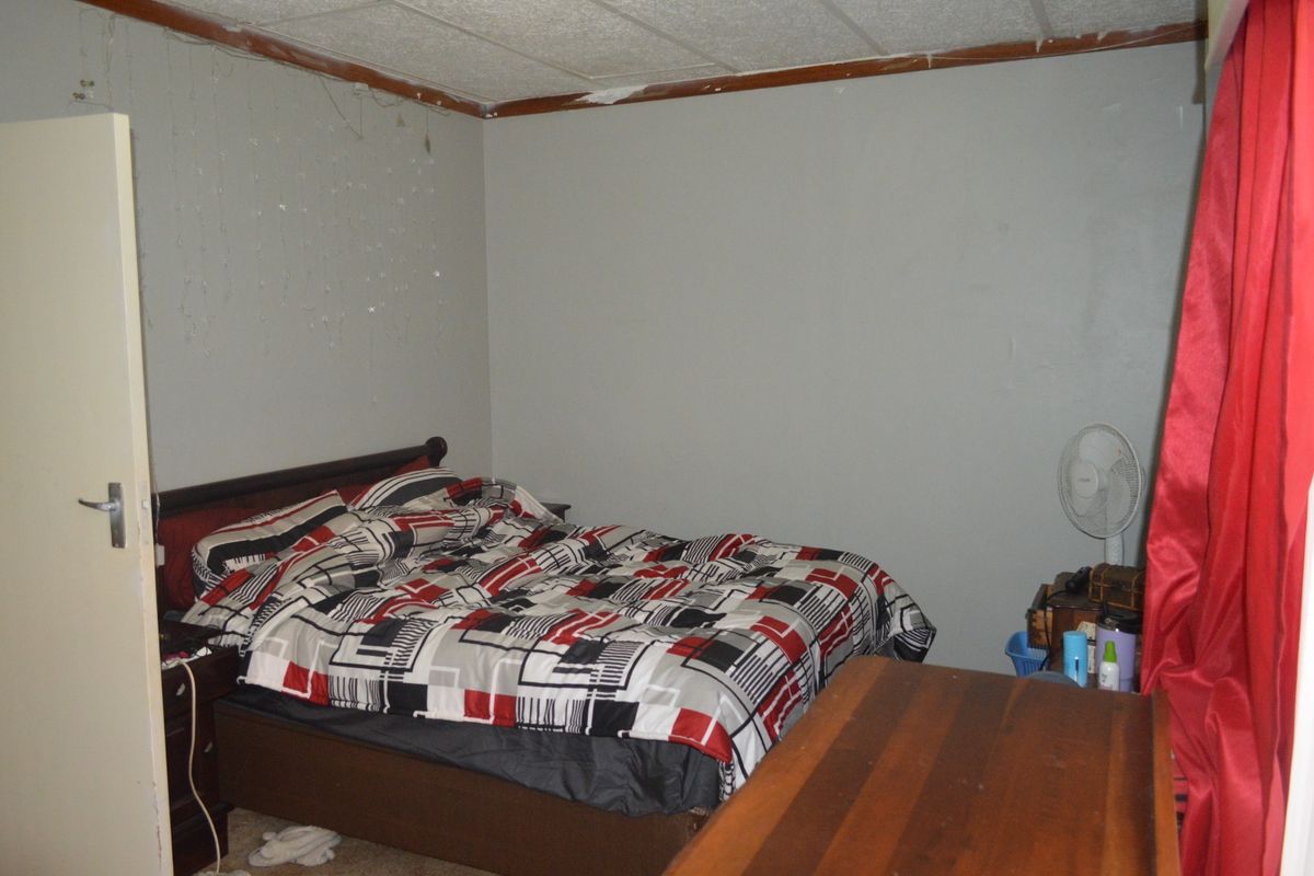 A bedroom featuring acoustic ceiling tiles and a standard door, currently requiring cosmetic updates to the ceiling and wall finishes.