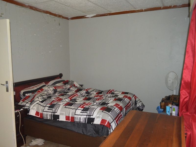 A bedroom featuring acoustic ceiling tiles and a standard door, currently requiring cosmetic updates to the ceiling and wall finishes.