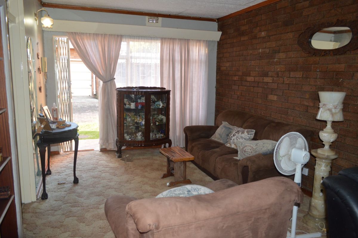 A living room featuring an exposed brick wall, carpeted flooring, and a sliding glass door providing access to the exterior.
