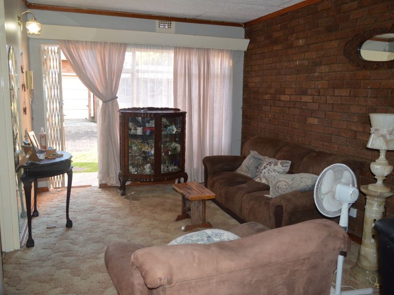 A living room featuring an exposed brick wall, carpeted flooring, and a sliding glass door providing access to the exterior.