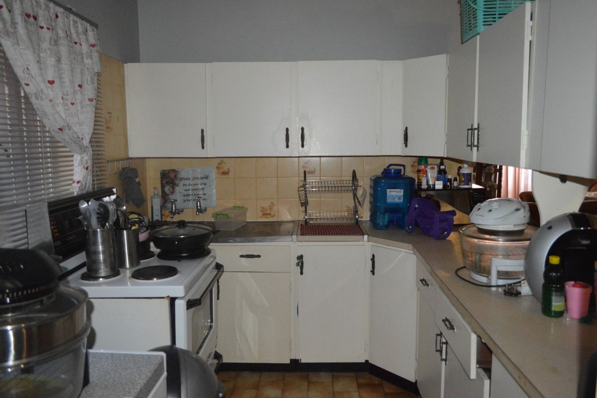 A dated kitchen featuring white cabinetry, tiled backsplash, and laminate countertops, requiring modernization to improve functionality and aesthetic appeal.