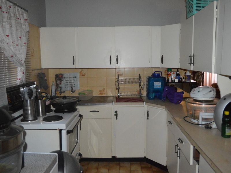 A dated kitchen featuring white cabinetry, tiled backsplash, and laminate countertops, requiring modernization to improve functionality and aesthetic appeal.