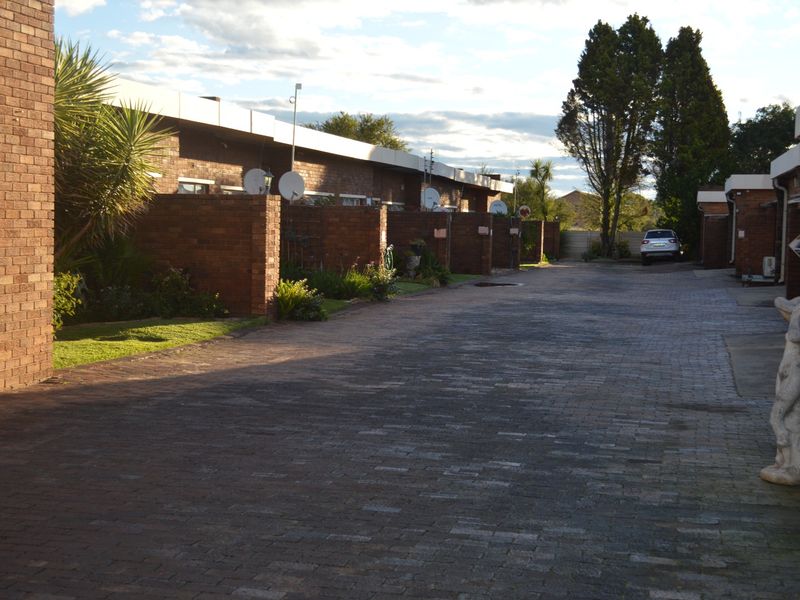 A view of the townhouse complex driveway featuring brick facades, paved surfaces, and individual unit boundary walls.