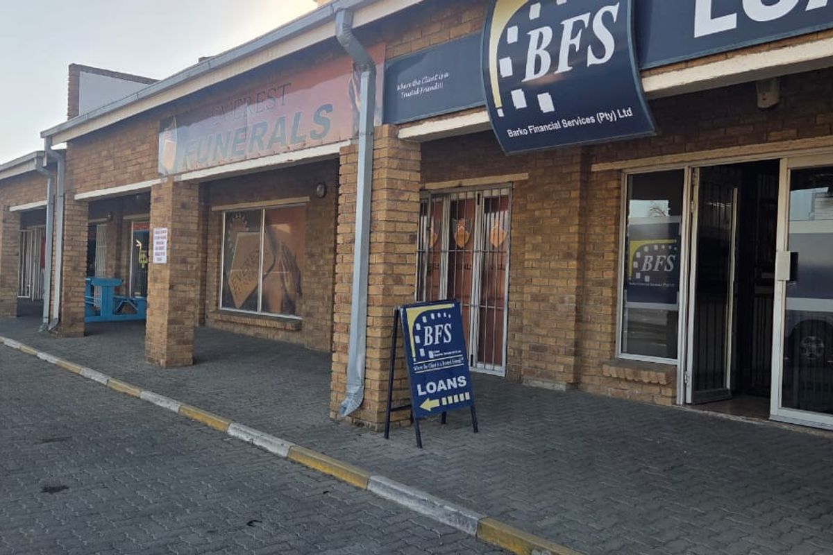 Front elevation of a commercial strip mall featuring face brick construction, paved walkway, and multiple storefront entrances with aluminum frames.