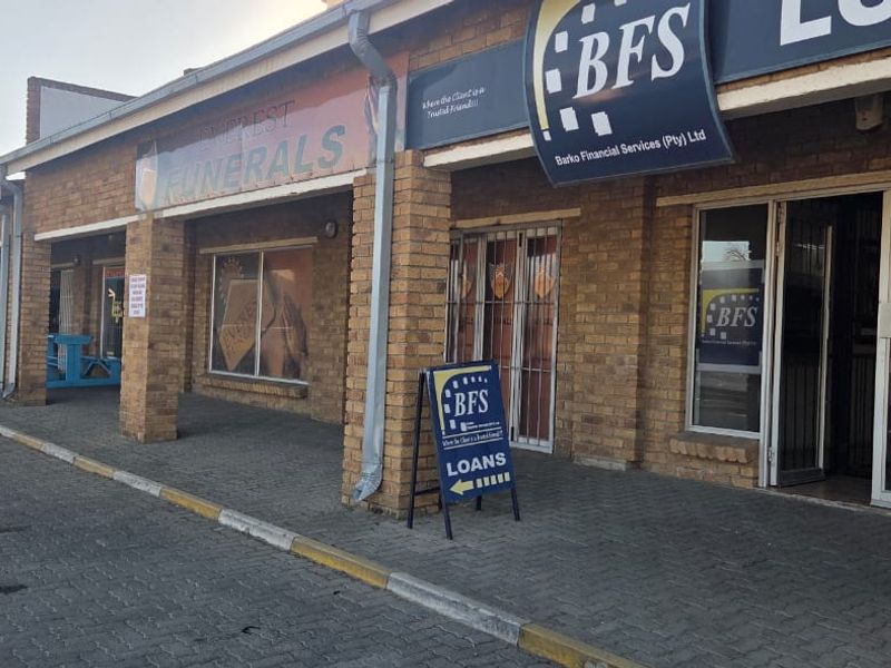 Front elevation of a commercial strip mall featuring face brick construction, paved walkway, and multiple storefront entrances with aluminum frames.