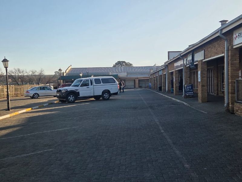 Exterior view of a commercial strip mall featuring a paved parking area, brick facade, and covered walkway access to storefronts.