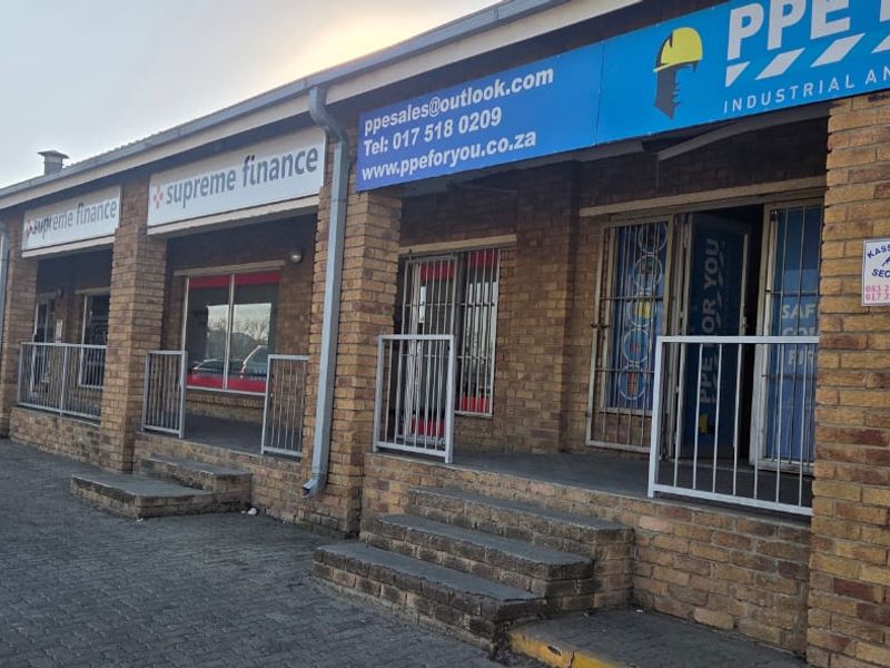 Front exterior view of a commercial strip mall featuring brick facade, security gates, and multiple storefronts with signage.