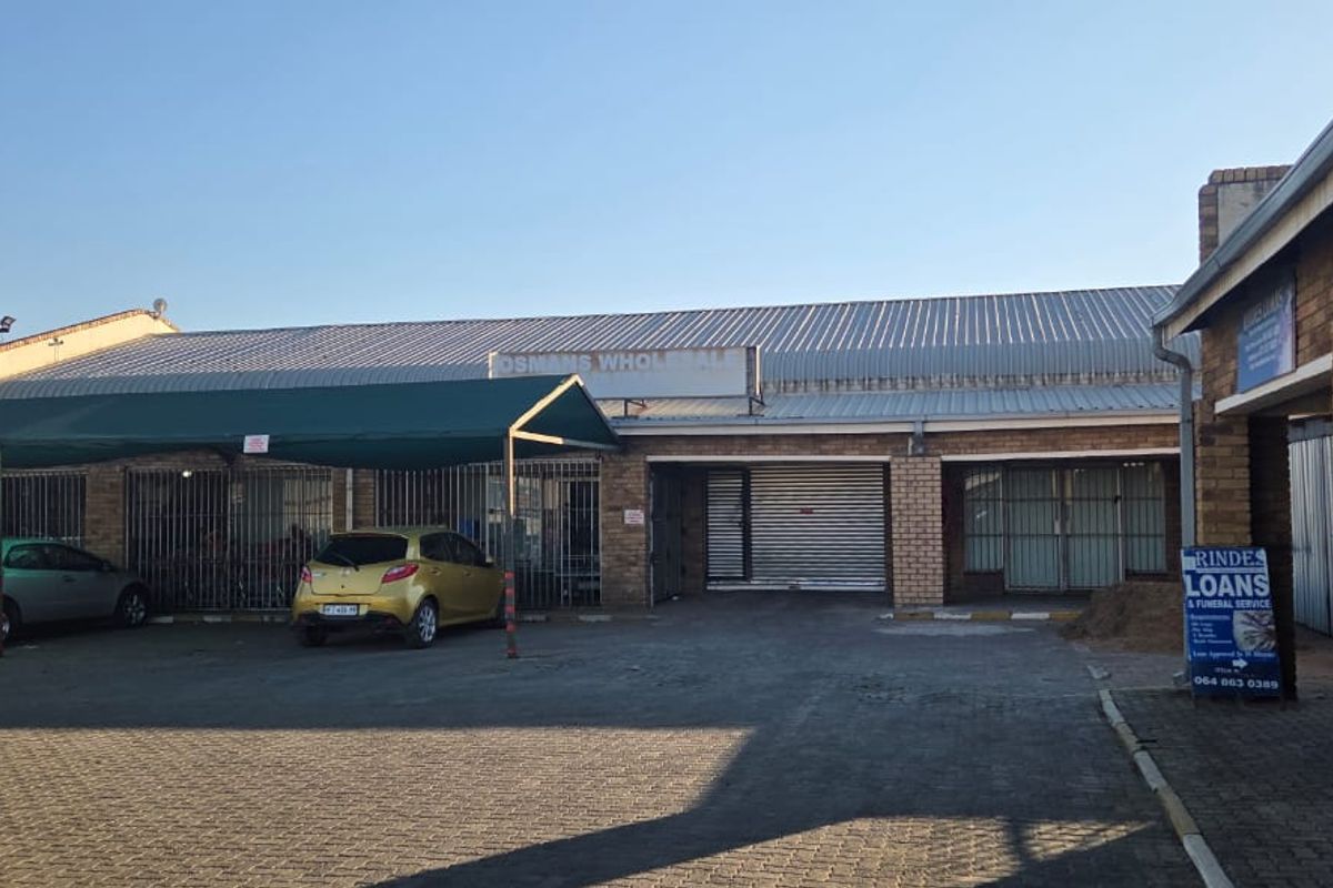 Commercial property frontage featuring brick construction, metal roofing, roller shutter access, and a paved parking area with a covered carport structure.