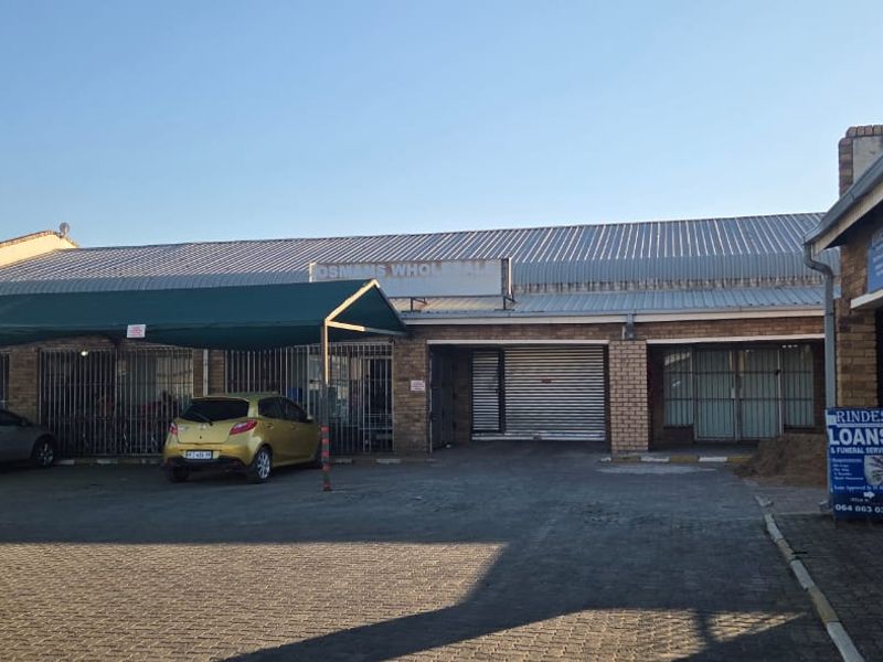Commercial property frontage featuring brick construction, metal roofing, roller shutter access, and a paved parking area with a covered carport structure.