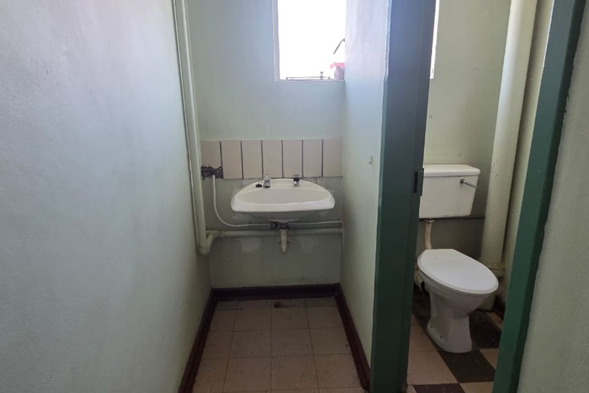 A dated bathroom featuring a wall-mounted basin and toilet with exposed plumbing, requiring renovation to modernize the finishes and fixtures.