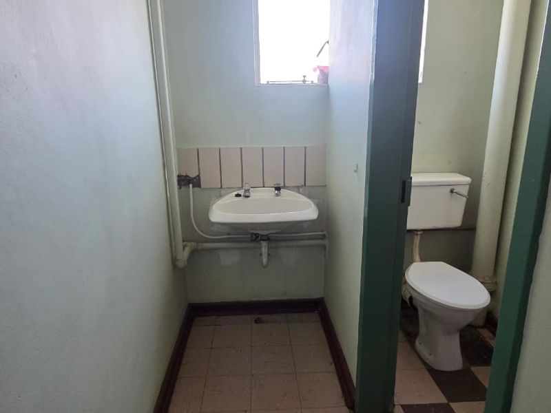 A dated bathroom featuring a wall-mounted basin and toilet with exposed plumbing, requiring renovation to modernize the finishes and fixtures.