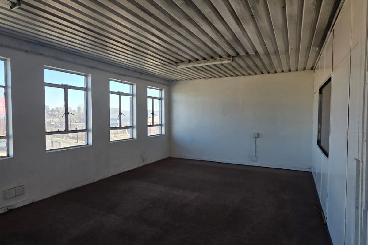 An empty, functional office space featuring large windows for natural light, a corrugated metal ceiling, and carpeted flooring.