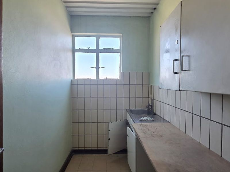 A functional scullery area featuring a stainless steel sink, tiled splashback, and built-in cabinetry, offering a practical space for utility and preparation tasks.