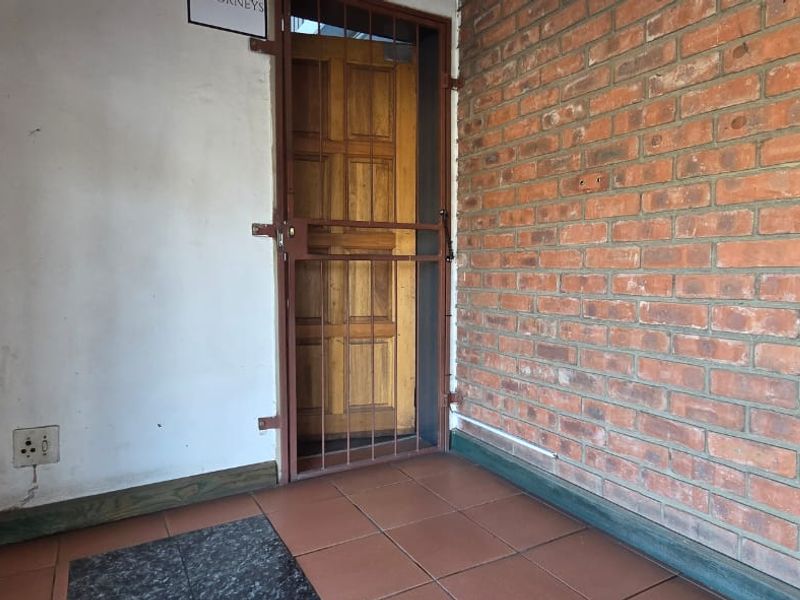 An entrance area featuring exposed brickwork, tiled flooring, and a secure metal gate over a timber door.
