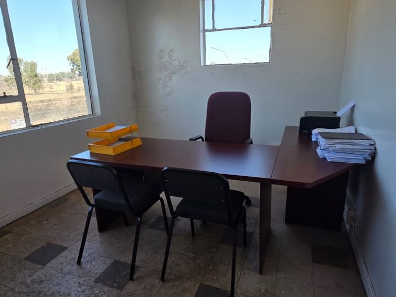 A functional office space featuring large windows for natural light and vinyl tile flooring, currently requiring cosmetic updates to the walls and finishes.