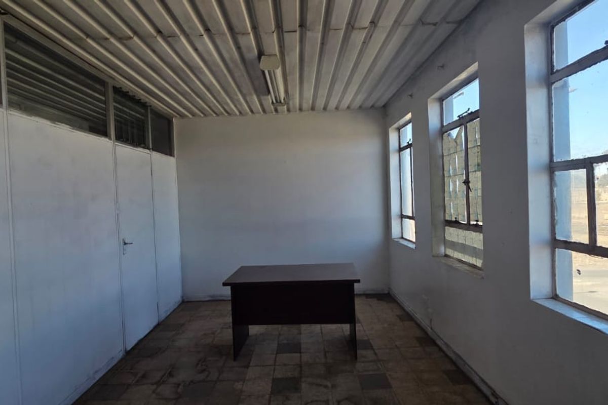 A vacant office space featuring a corrugated metal ceiling, large steel-framed windows, and partition walling, offering a functional layout for commercial use.
