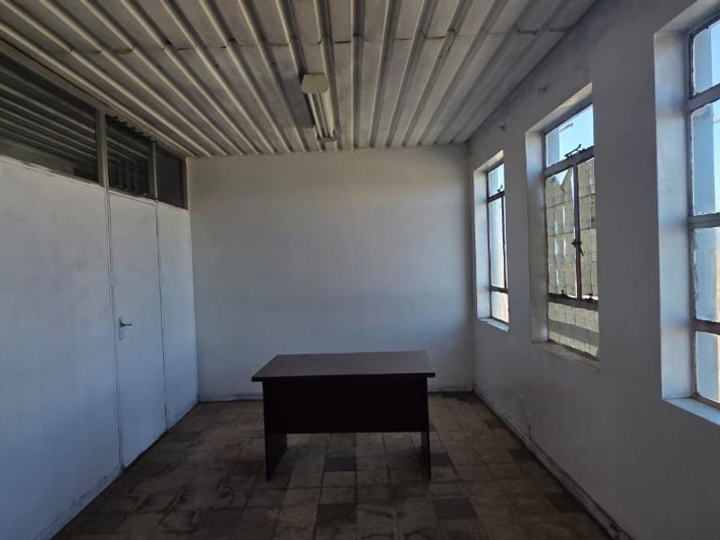 A vacant office space featuring a corrugated metal ceiling, large steel-framed windows, and partition walling, offering a functional layout for commercial use.