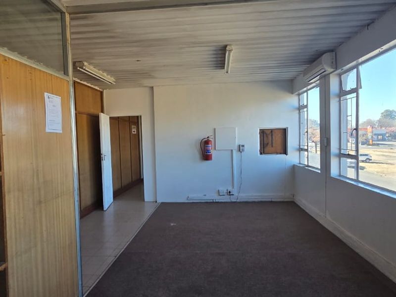 Vacant commercial office space featuring large windows, built-in shelving, and wall-mounted air conditioning, requiring cosmetic updates to flooring and wall finishes.