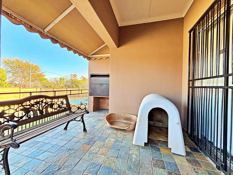 Covered patio area featuring tiled flooring, a built-in braai, and a security gate, providing a functional outdoor space for entertaining.