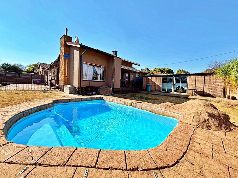 Rear exterior view featuring a swimming pool with stone-look coping, brick chimney, and a paved backyard area with boundary walling.