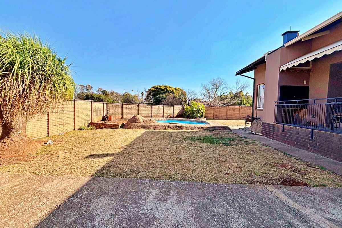Rear garden area featuring a swimming pool, brick boundary walls, and a covered patio space with metal railings.