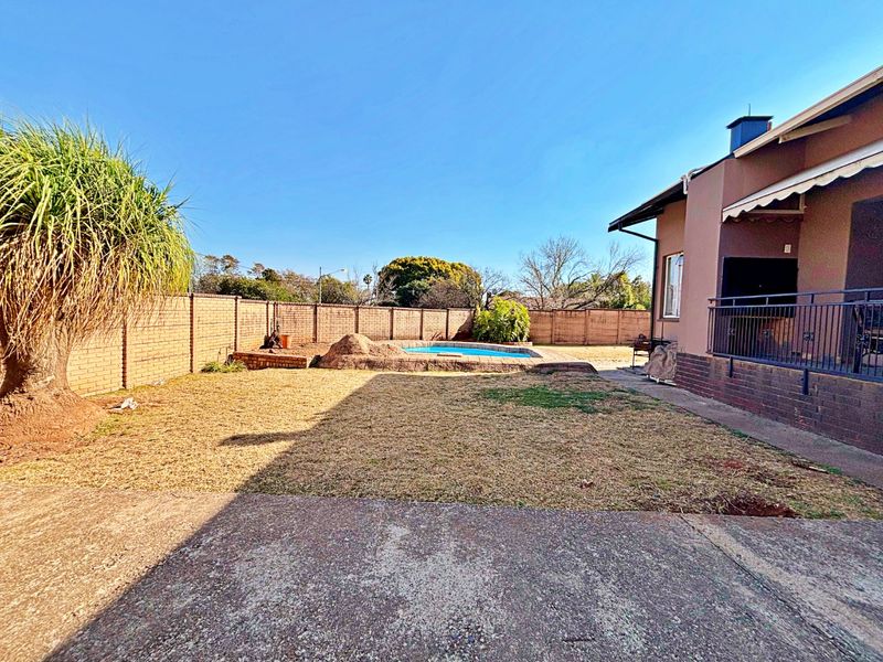 Rear garden area featuring a swimming pool, brick boundary walls, and a covered patio space with metal railings.
