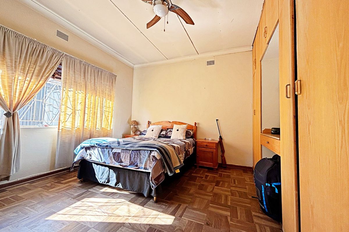 A bedroom featuring classic parquet flooring, built-in wooden cupboards, and a ceiling fan, offering a functional space with potential for modernization.