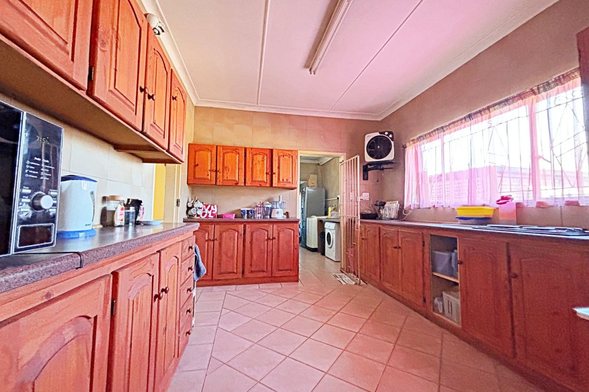 A functional kitchen featuring extensive timber cabinetry, laminate countertops, tiled flooring, and a direct view into the adjacent laundry area.