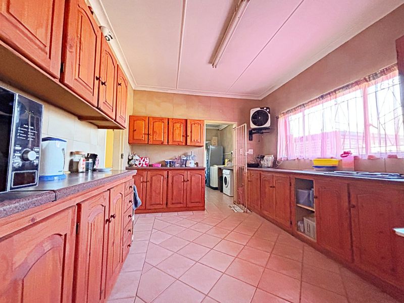 A functional kitchen featuring extensive timber cabinetry, laminate countertops, tiled flooring, and a direct view into the adjacent laundry area.