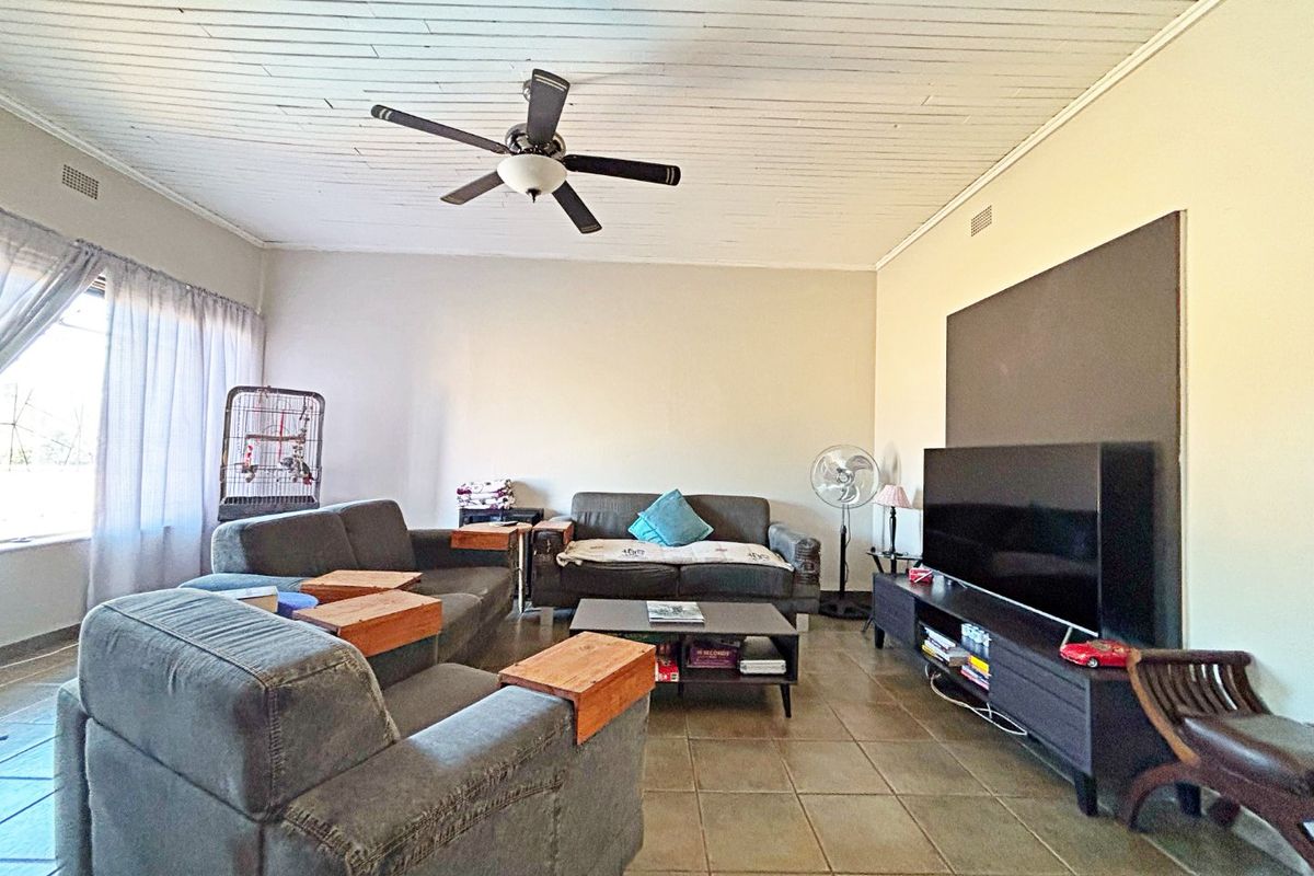 Spacious living room featuring tiled flooring, a timber panelled ceiling, and a central ceiling fan, providing a comfortable and functional family living space.