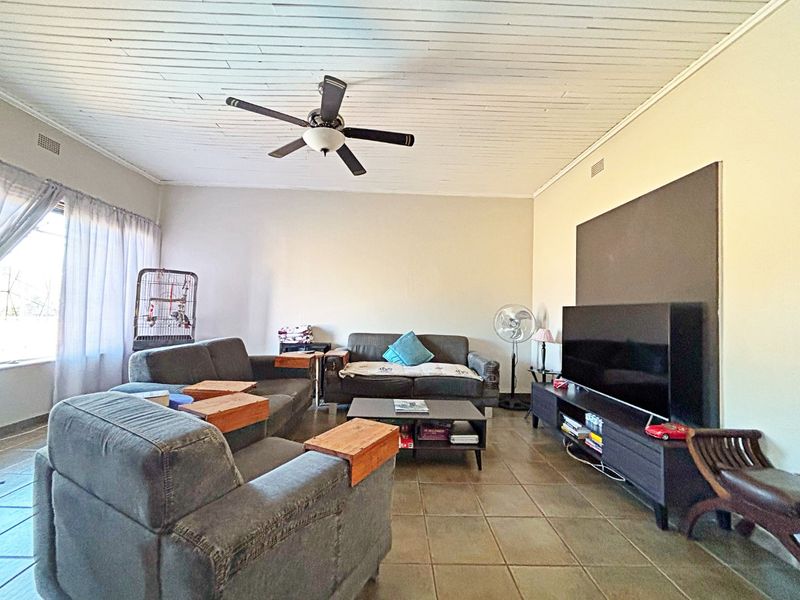 Spacious living room featuring tiled flooring, a timber panelled ceiling, and a central ceiling fan, providing a comfortable and functional family living space.