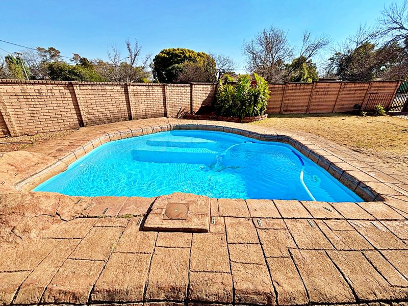 Outdoor swimming pool area featuring a paved surround and a high brick boundary wall for privacy.