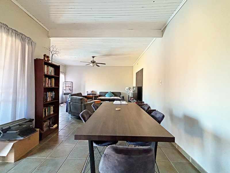 Spacious open-plan living and dining area featuring tiled flooring and an exposed beam ceiling with a central ceiling fan.
