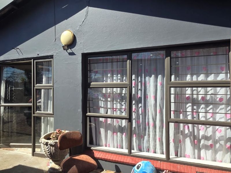 Rear exterior view of the property featuring dark painted walls, aluminium window frames with security bars, and a sliding door access point.