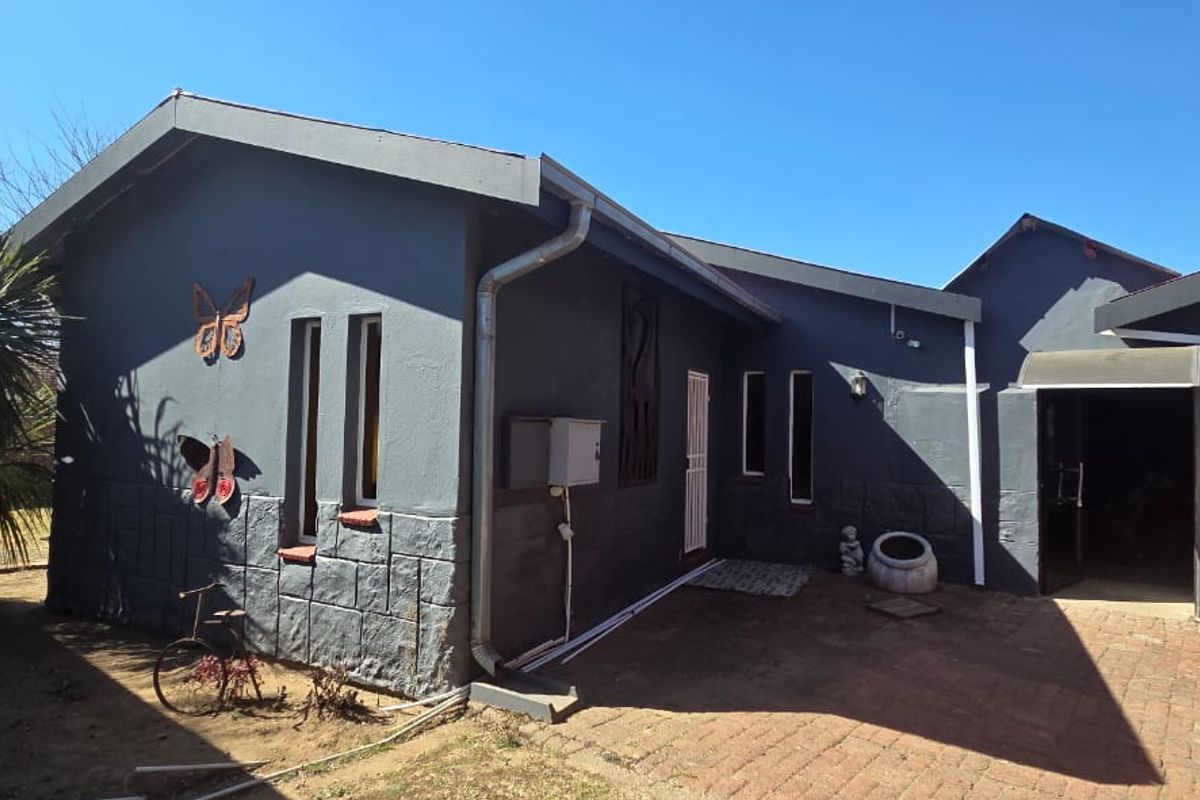 Rear exterior view of the house featuring dark painted walls with stone cladding accents, brick paved courtyard, and functional guttering systems.