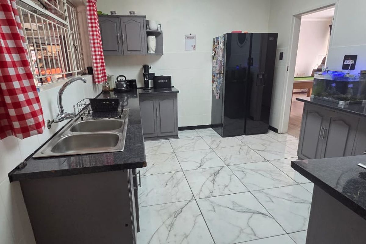 A functional kitchen featuring granite countertops, double basin sink, ample built-in cabinetry, and modern marble-look tiled flooring.
