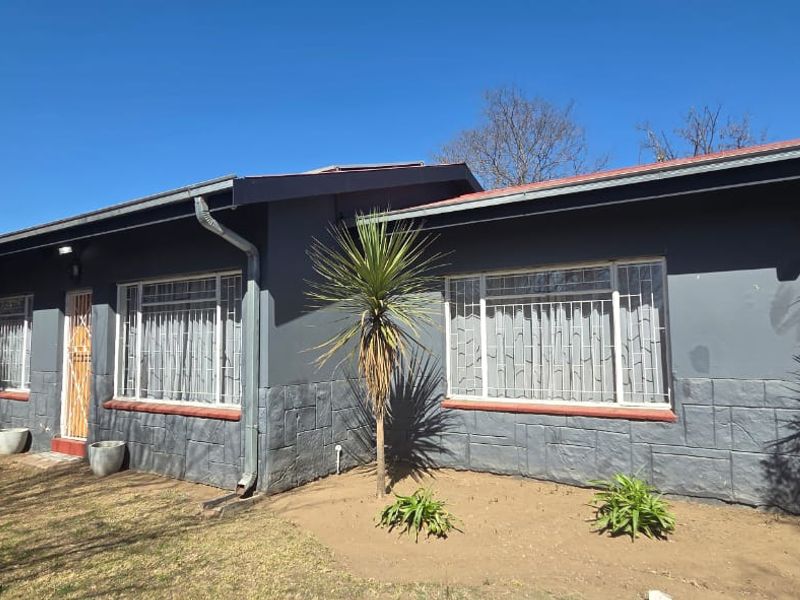 Front elevation of a single-story house featuring dark grey painted walls, textured stone-effect base cladding, and metal security bars on windows.
