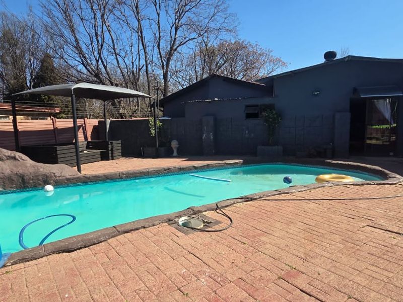 Outdoor pool area featuring a swimming pool with a slide, paved patio space, and a gazebo, set against a private boundary wall.