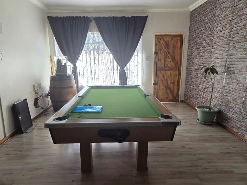A living area featuring laminate flooring and a rustic exposed brick feature wall, currently utilized as a recreational space.