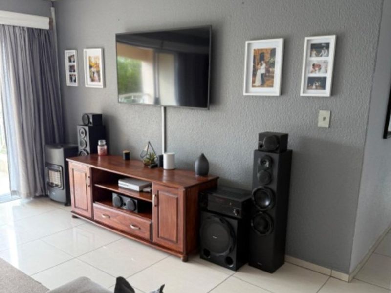 A well-maintained living room featuring neutral tiled flooring, coving, and a large sliding glass door providing access to the outdoor area.