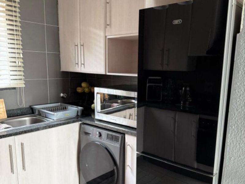 Compact kitchen featuring light wood-finish cabinetry, dark granite countertops, tiled backsplash, and integrated space for laundry appliances.