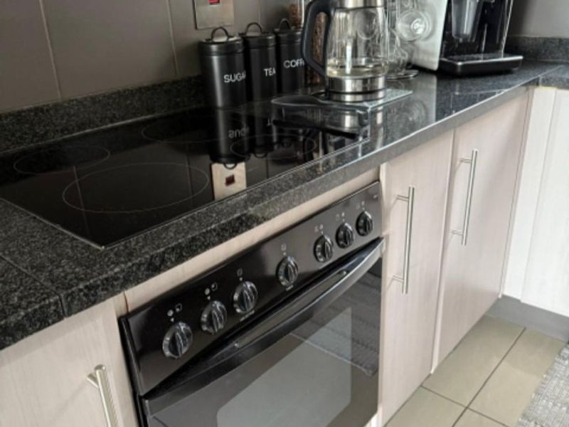 Modern kitchen featuring a sleek electric hob, built-in oven, granite countertops, and neutral cabinetry with tiled flooring.
