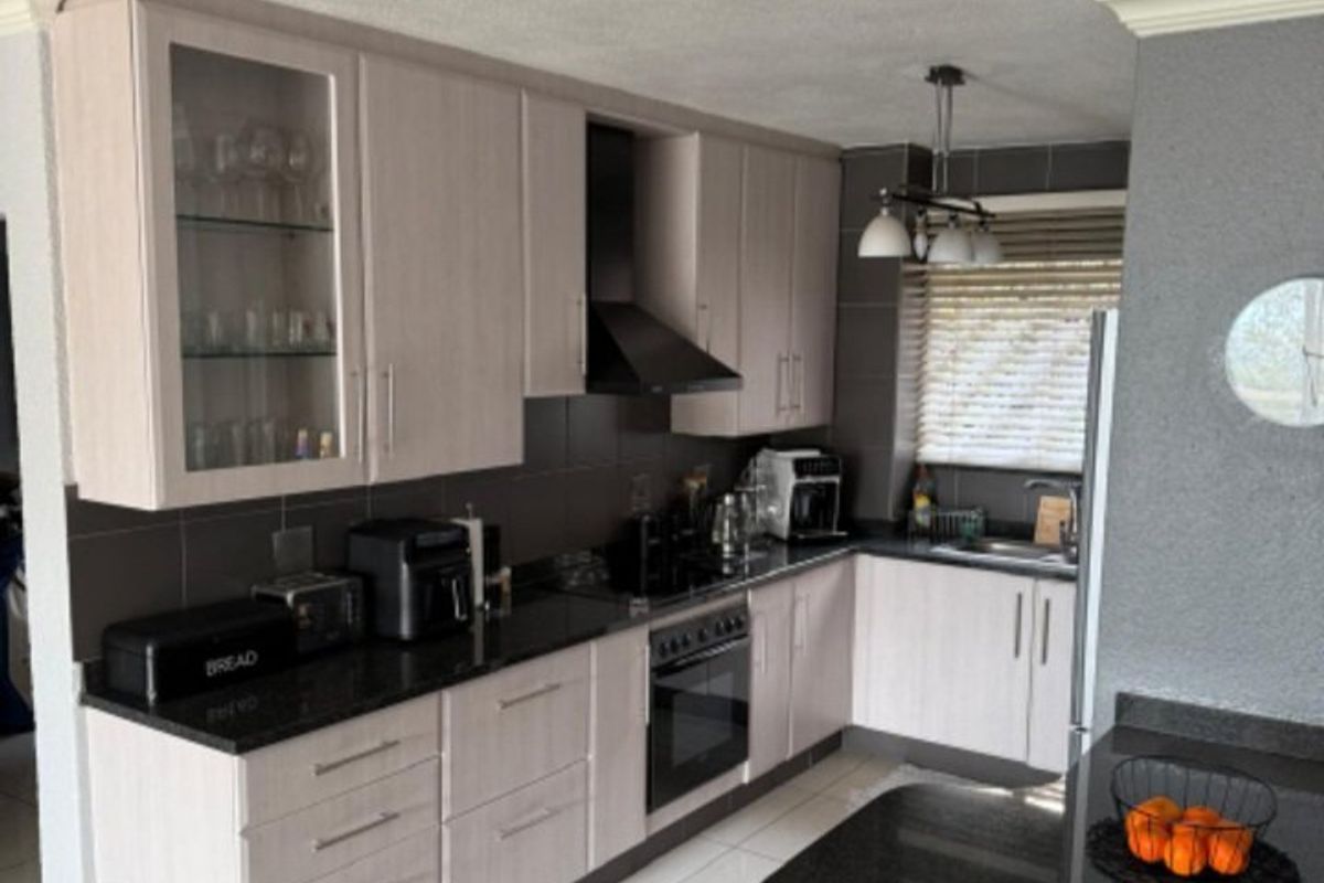 A well-maintained kitchen featuring light wood-finish cabinetry, dark granite countertops, integrated appliances, and a functional breakfast bar area with tiled flooring.