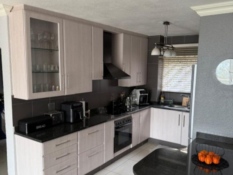 A well-maintained kitchen featuring light wood-finish cabinetry, dark granite countertops, integrated appliances, and a functional breakfast bar area with tiled flooring.