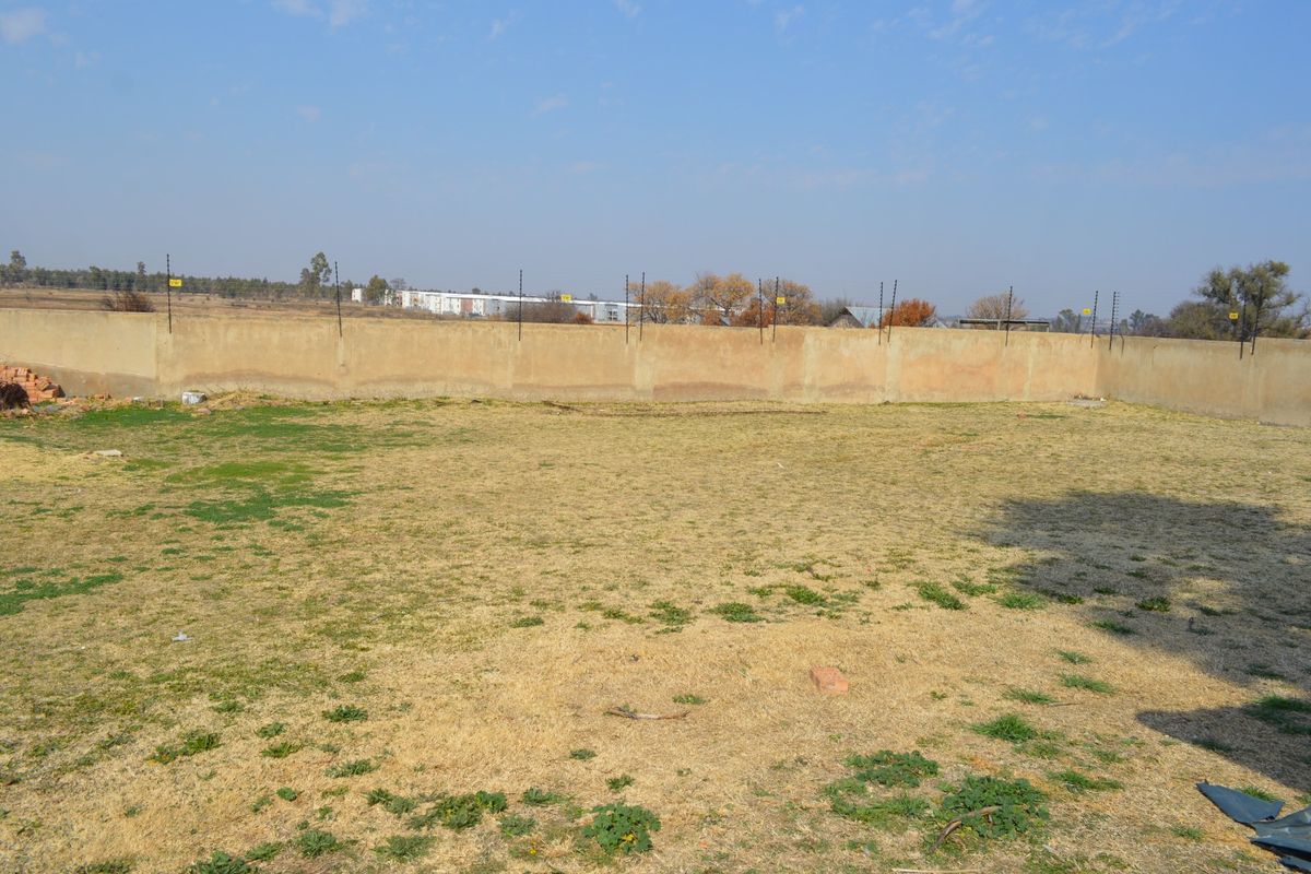 A vacant residential plot featuring a perimeter wall with installed electric fencing and an open grassed area.